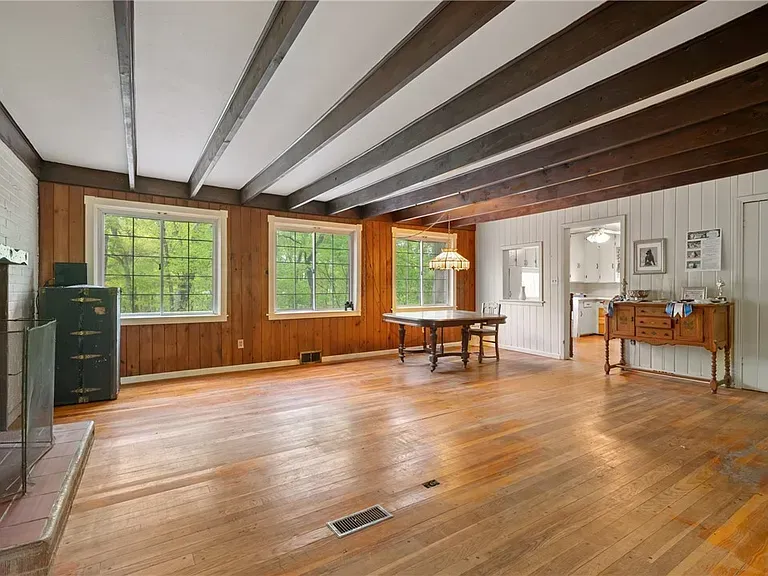 Empty rustic room with wood floors, exposed beams, large windows, and a small desk by the wall