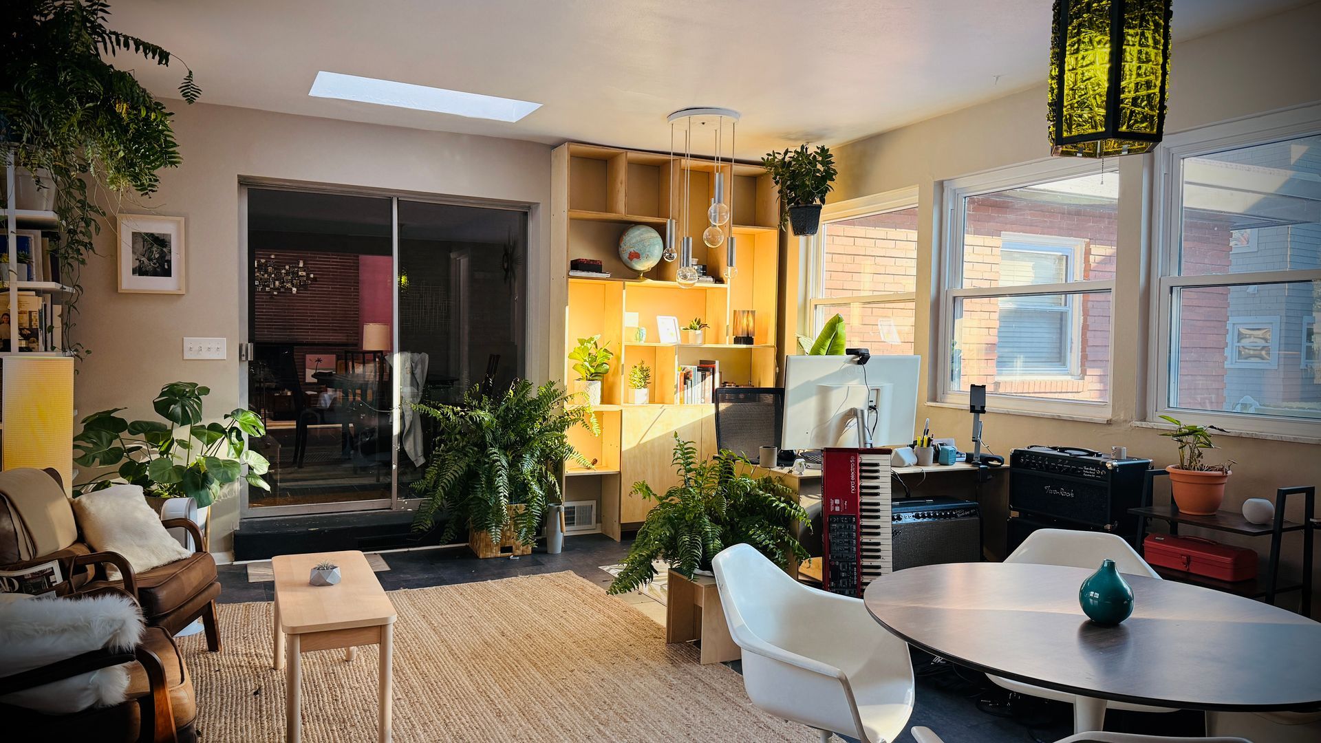Cozy modern living room with plants, warm lighting, a sofa, dining table, and large window.