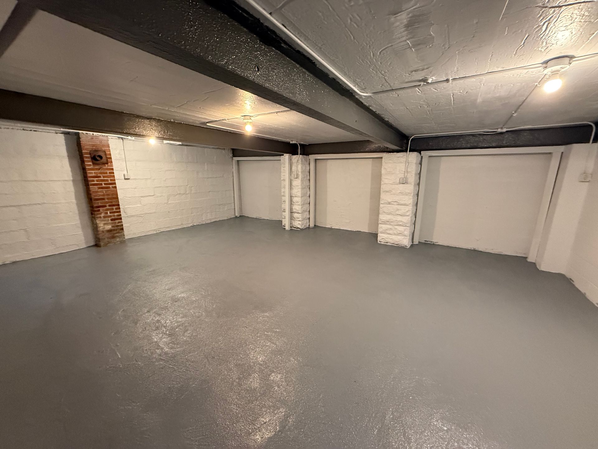 Empty gray basement room with white cinder block walls, exposed beams, and a support post