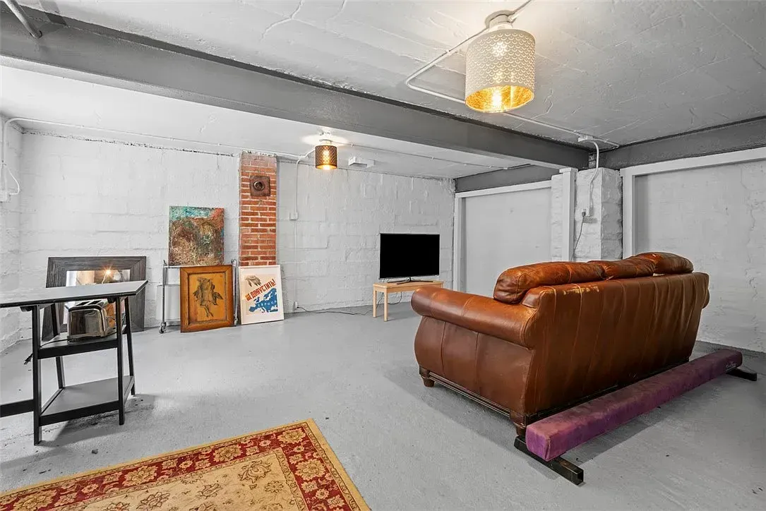 Modern basement living room with a brown leather sofa, TV, wall art, and small table on a gray floor