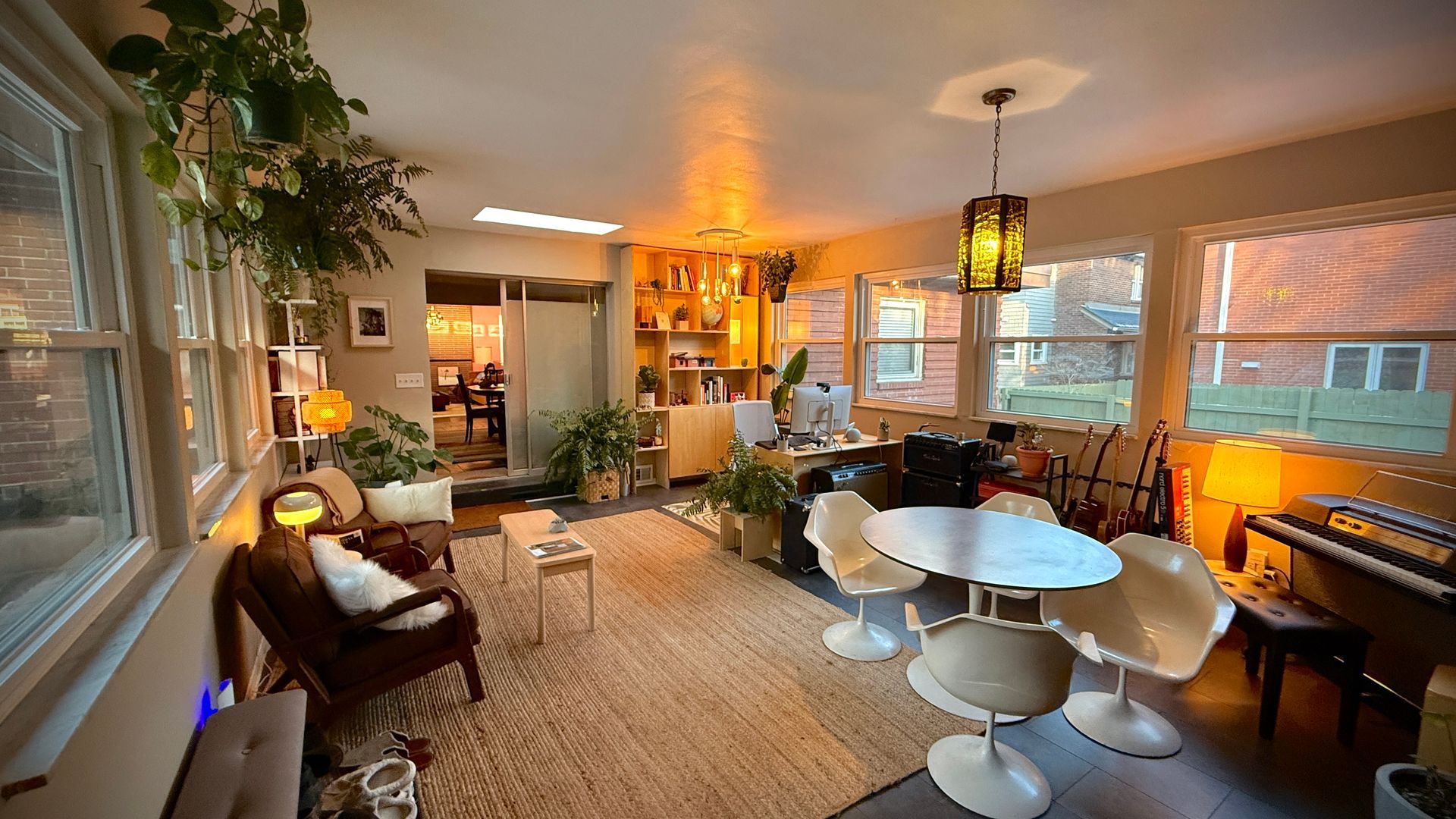 Cozy sunroom with wicker chairs, round table, hanging lantern, and large windows overlooking a yard.