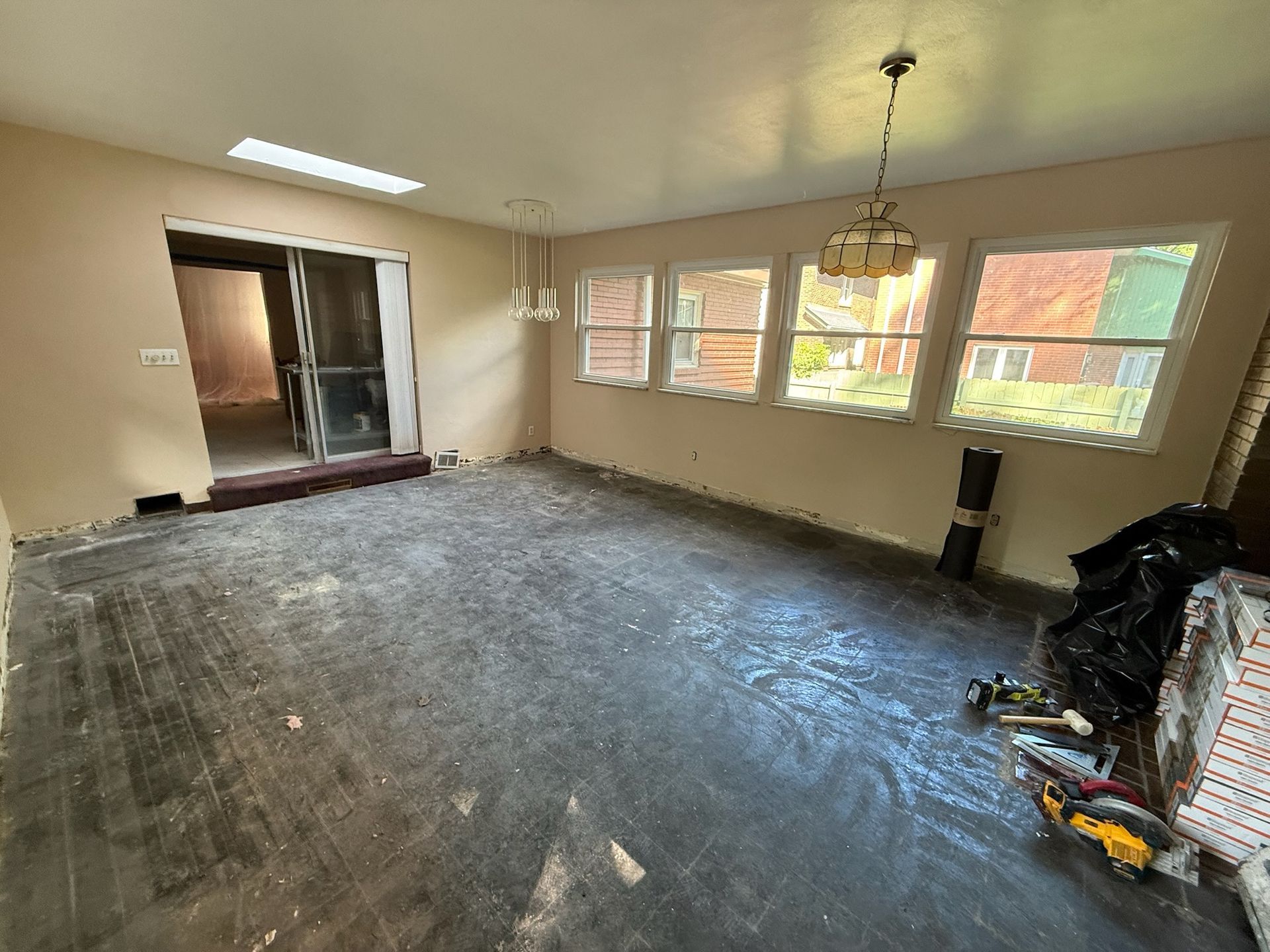 Empty living room with bare concrete floor, beige walls, windows, and a hanging light fixture