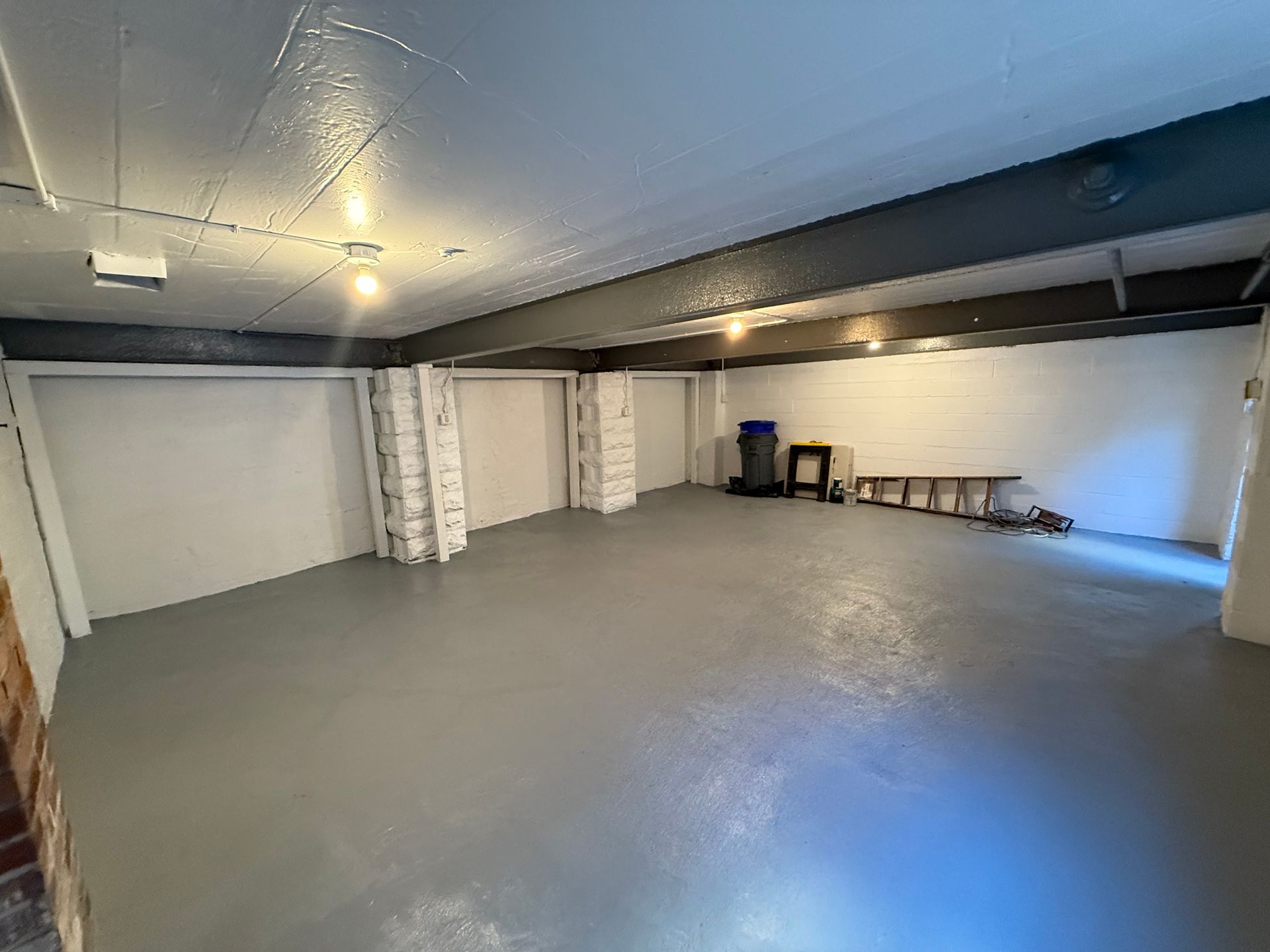 Empty gray garage or basement with white walls, ceiling lights, and a few stored items along the back wall