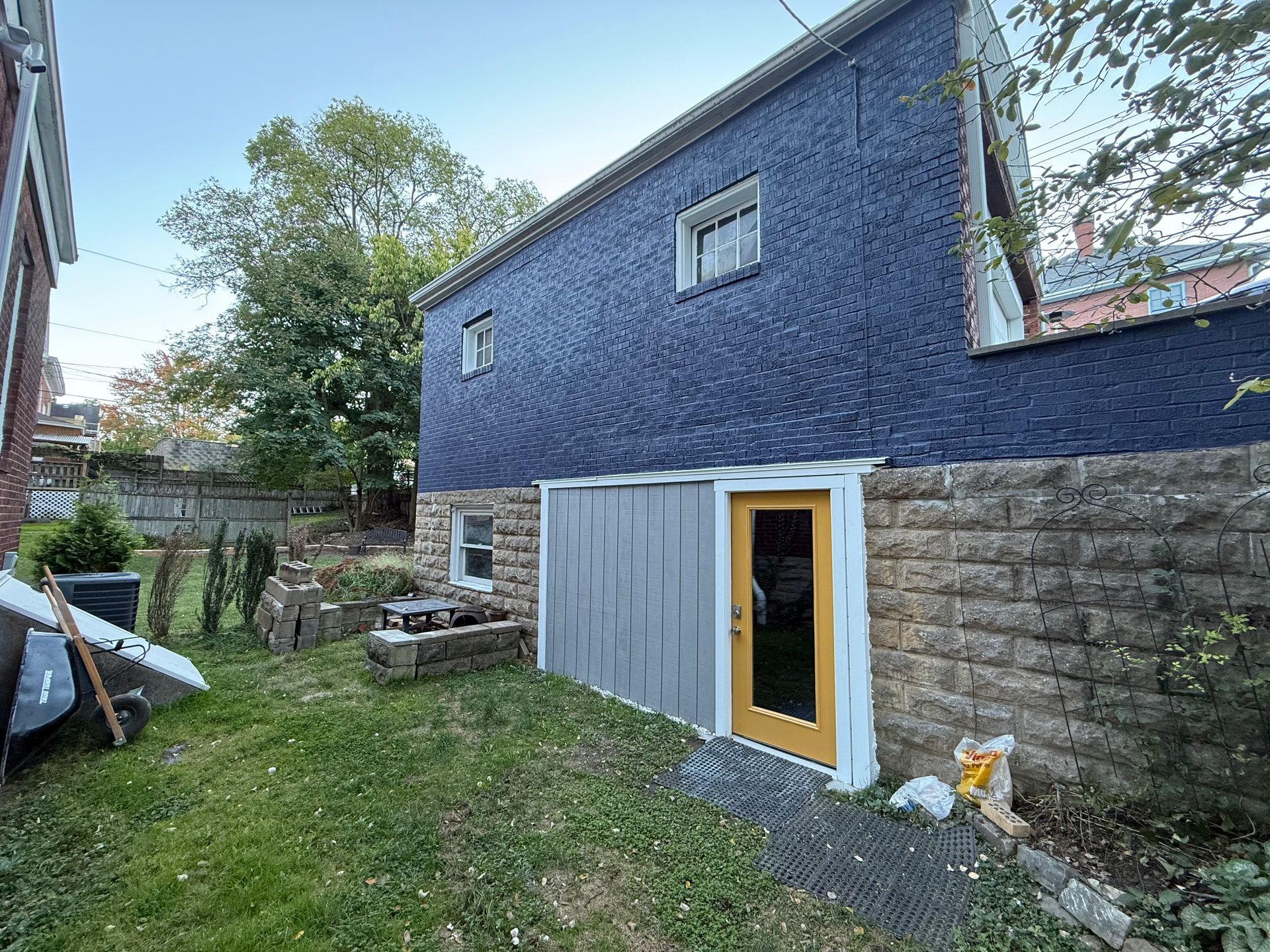 Backyard with blue house exterior, stone wall, grass, and a small door with yellow trim