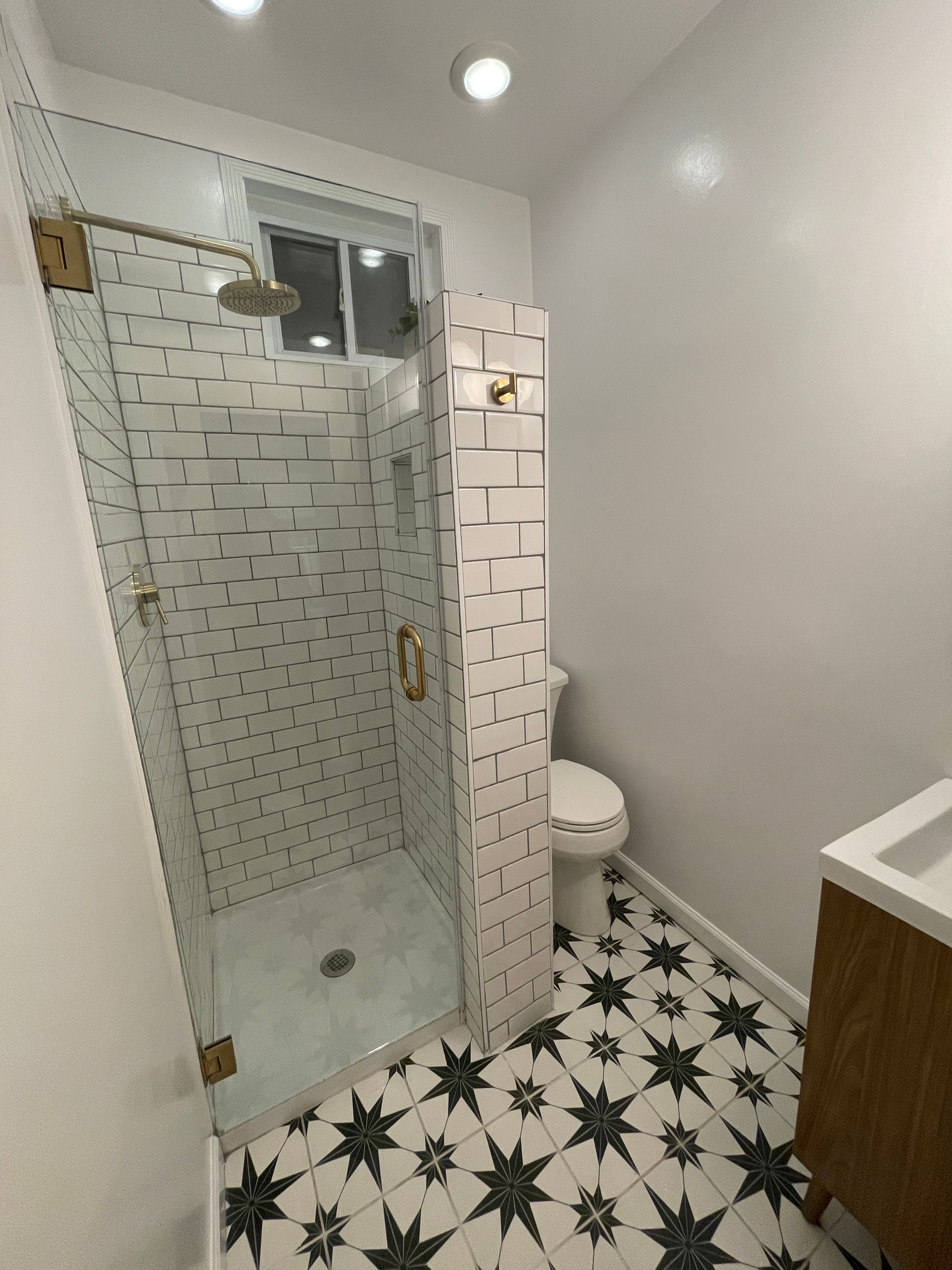 Modern bathroom with glass shower, white subway tile, black star-pattern floor, and wood vanity