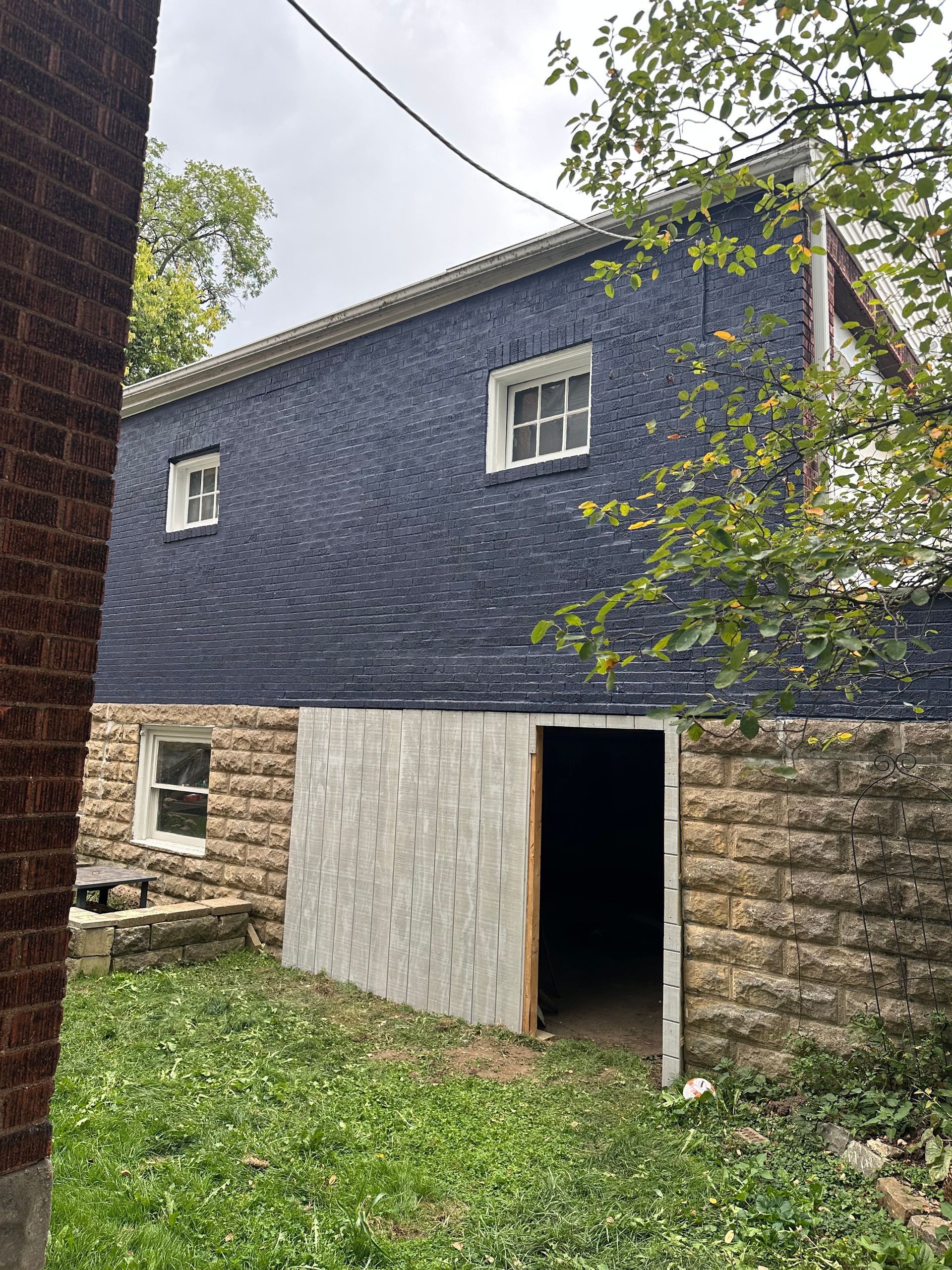 Stone barn with dark blue siding, small windows, and open doorway in a grassy yard