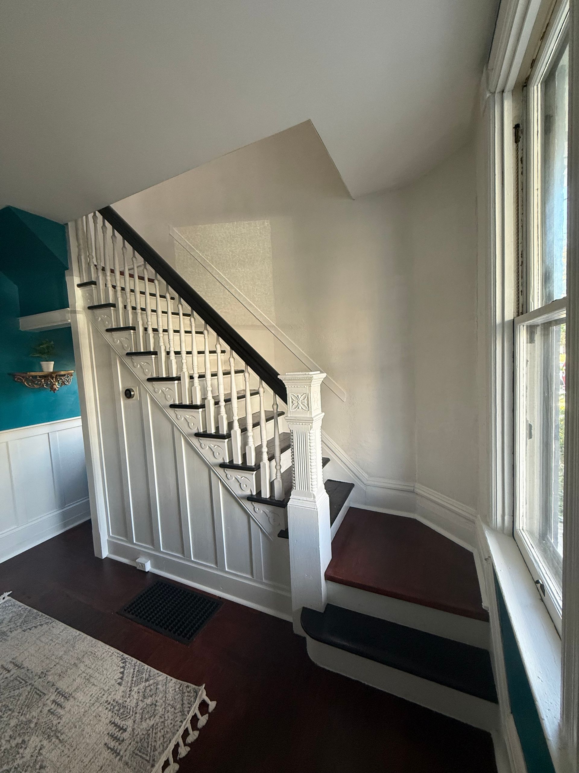 Staircase with white railings beside a window in a bright entryway.