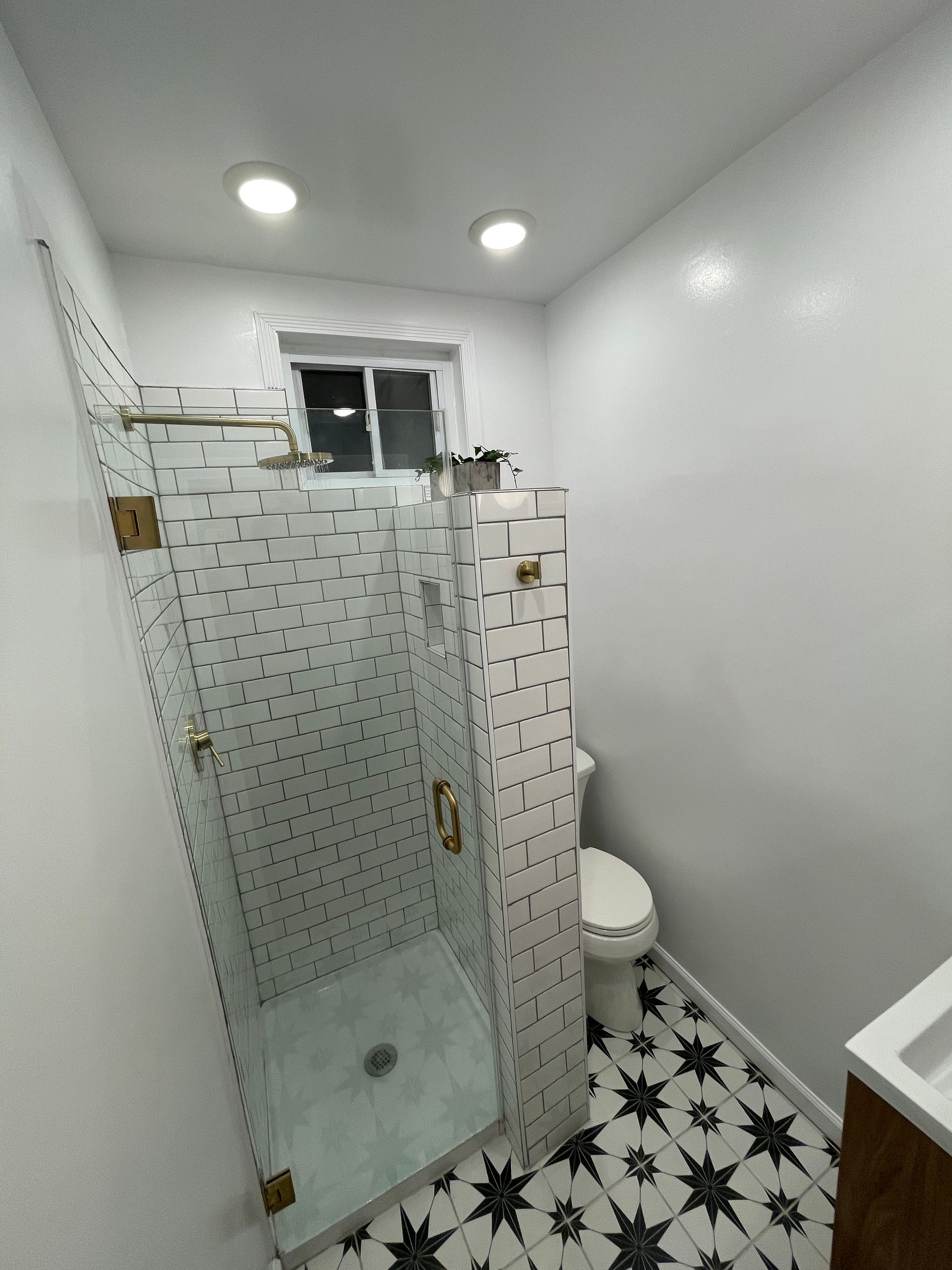 Small bathroom with glass shower, mosaic floor, toilet, and bright white walls.