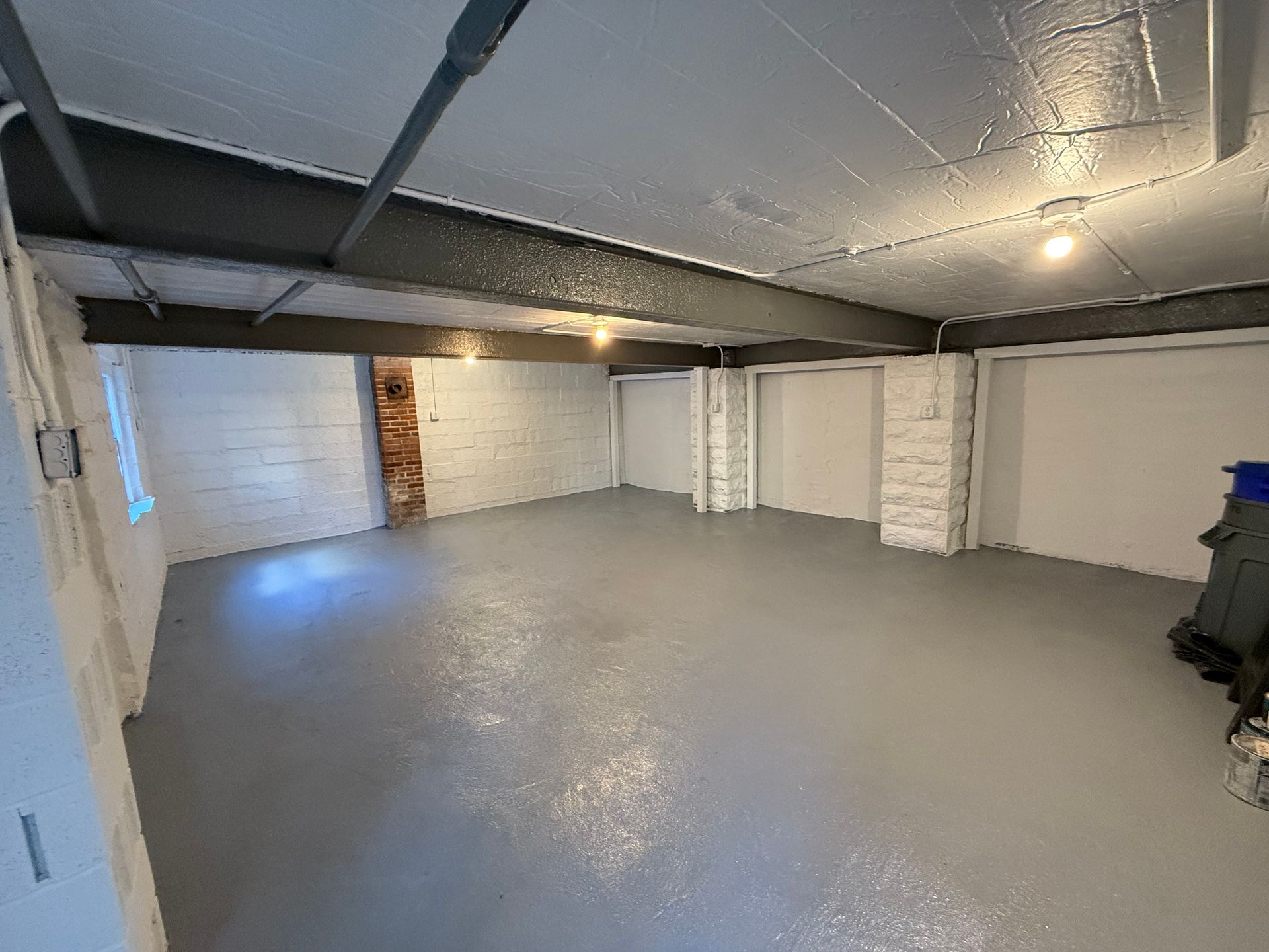 Empty white basement garage with gray floor and exposed ceiling beams