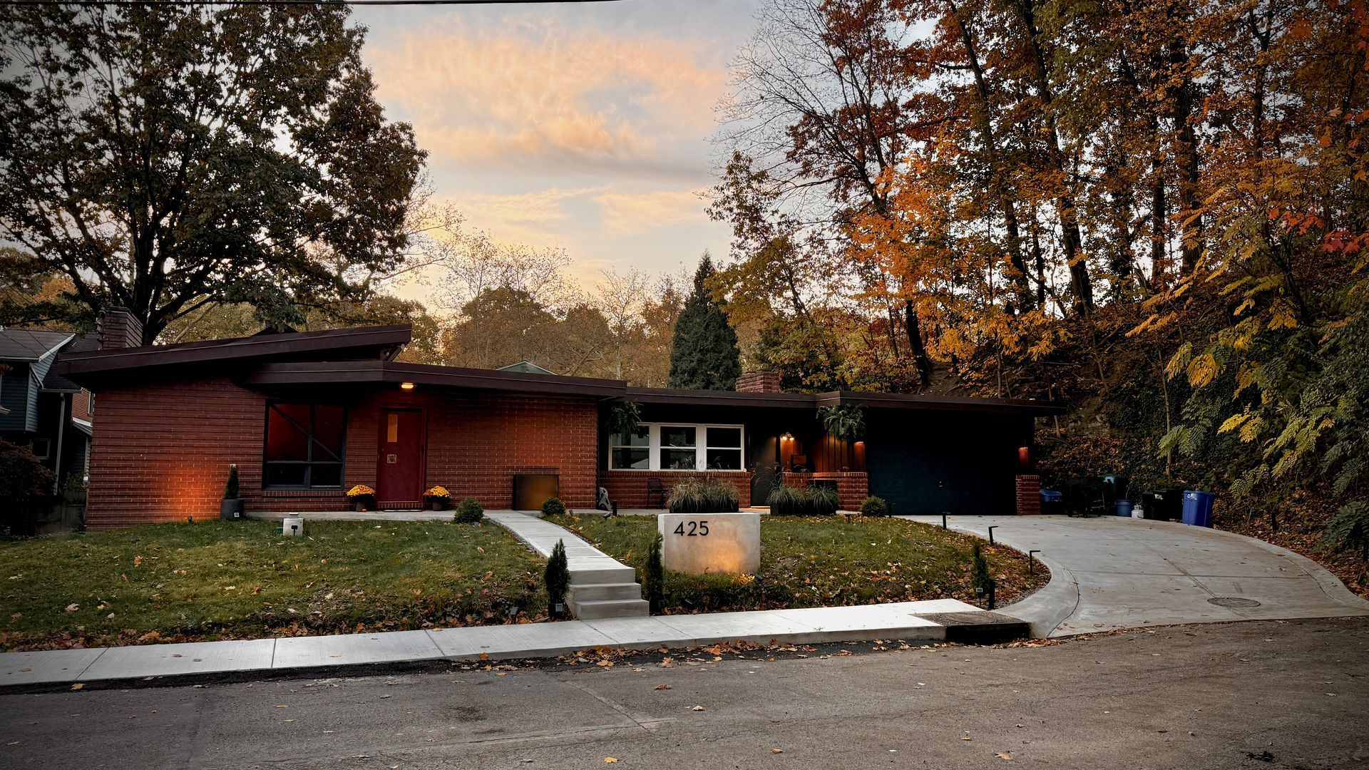 Single-story brick house with a curved driveway and autumn trees at dusk
