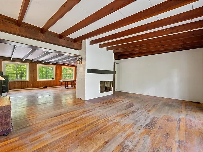 Spacious empty living room with wood floors, exposed beams, fireplace, and large windows