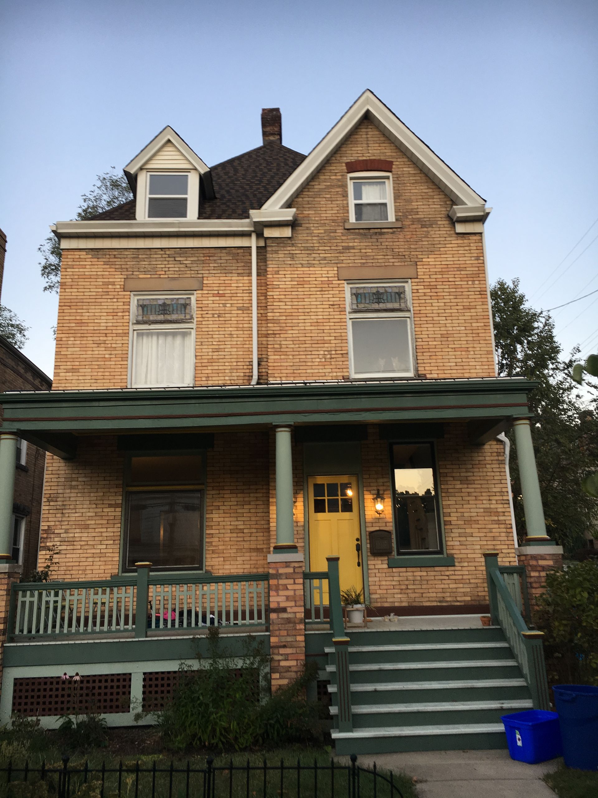 Two-story brick house with green porch, yellow front door, and dormer windows