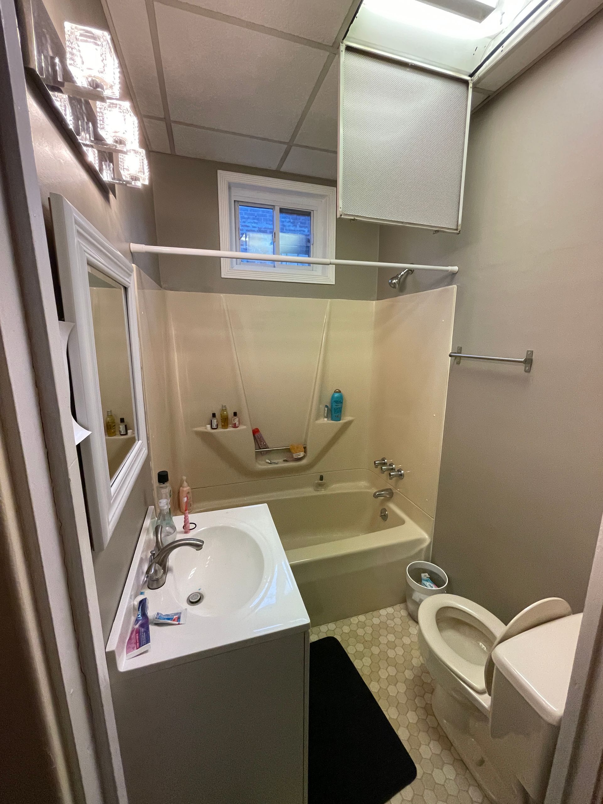 Small beige bathroom with sink, toilet, bathtub, shower curtain, and window.