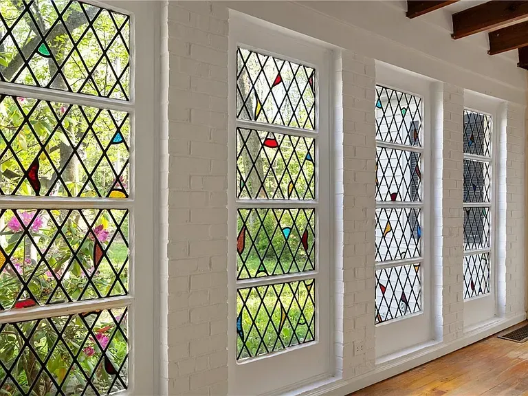Sunlit interior with white-framed leaded-glass windows and garden greenery outside