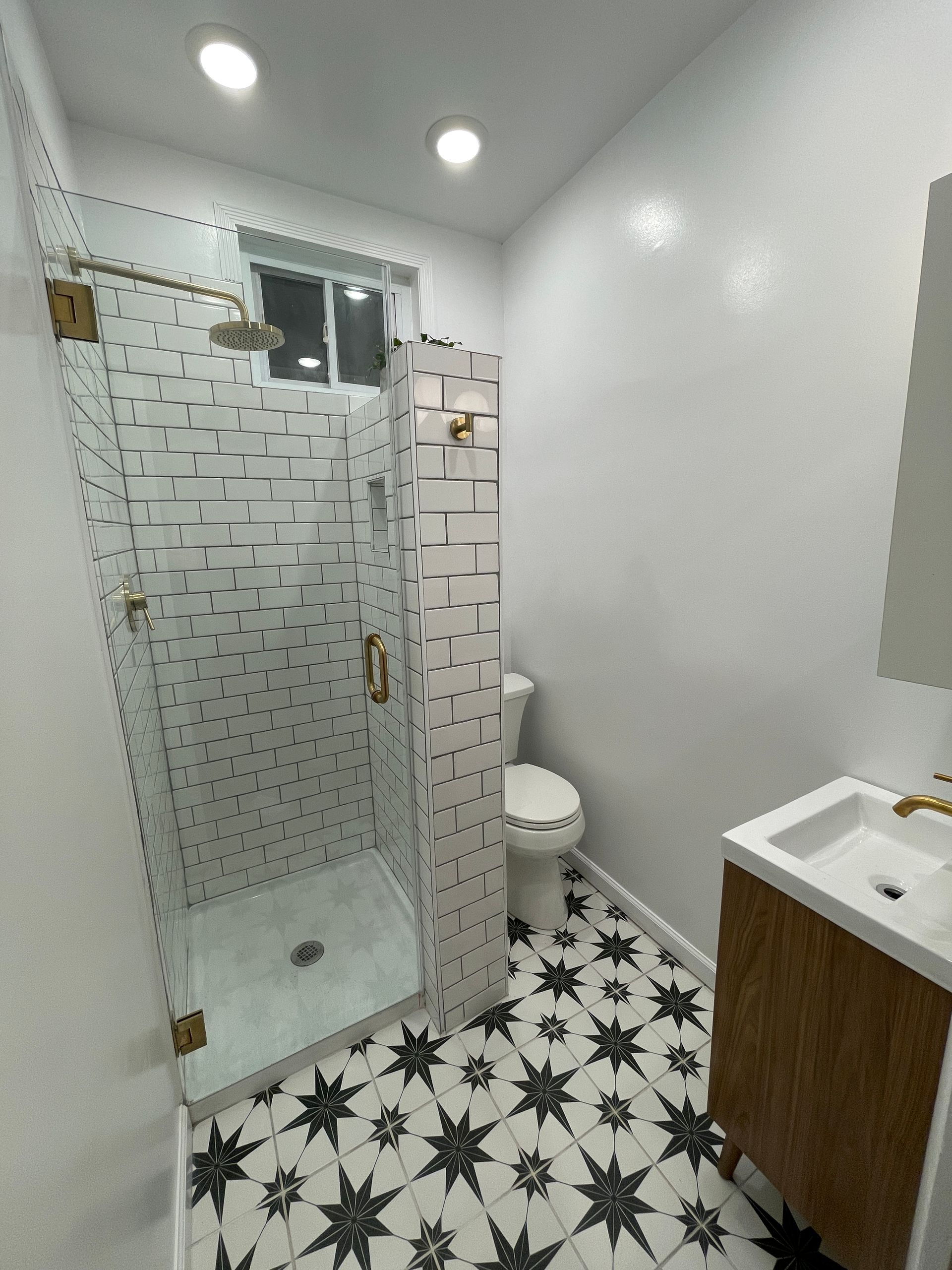 Small bathroom with glass shower, toilet, white sink vanity, and black-and-white patterned floor tiles.