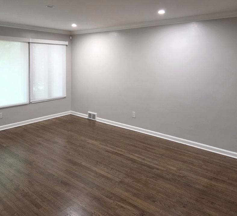 Empty living room with gray walls, wood floors, and large windows with blinds