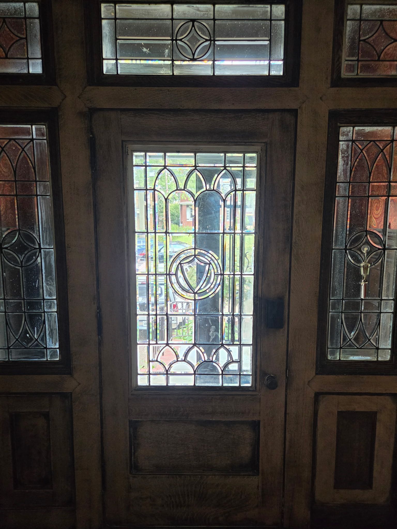 Front door with decorative stained glass panels and sidelights, looking out to a sunlit porch and garden.