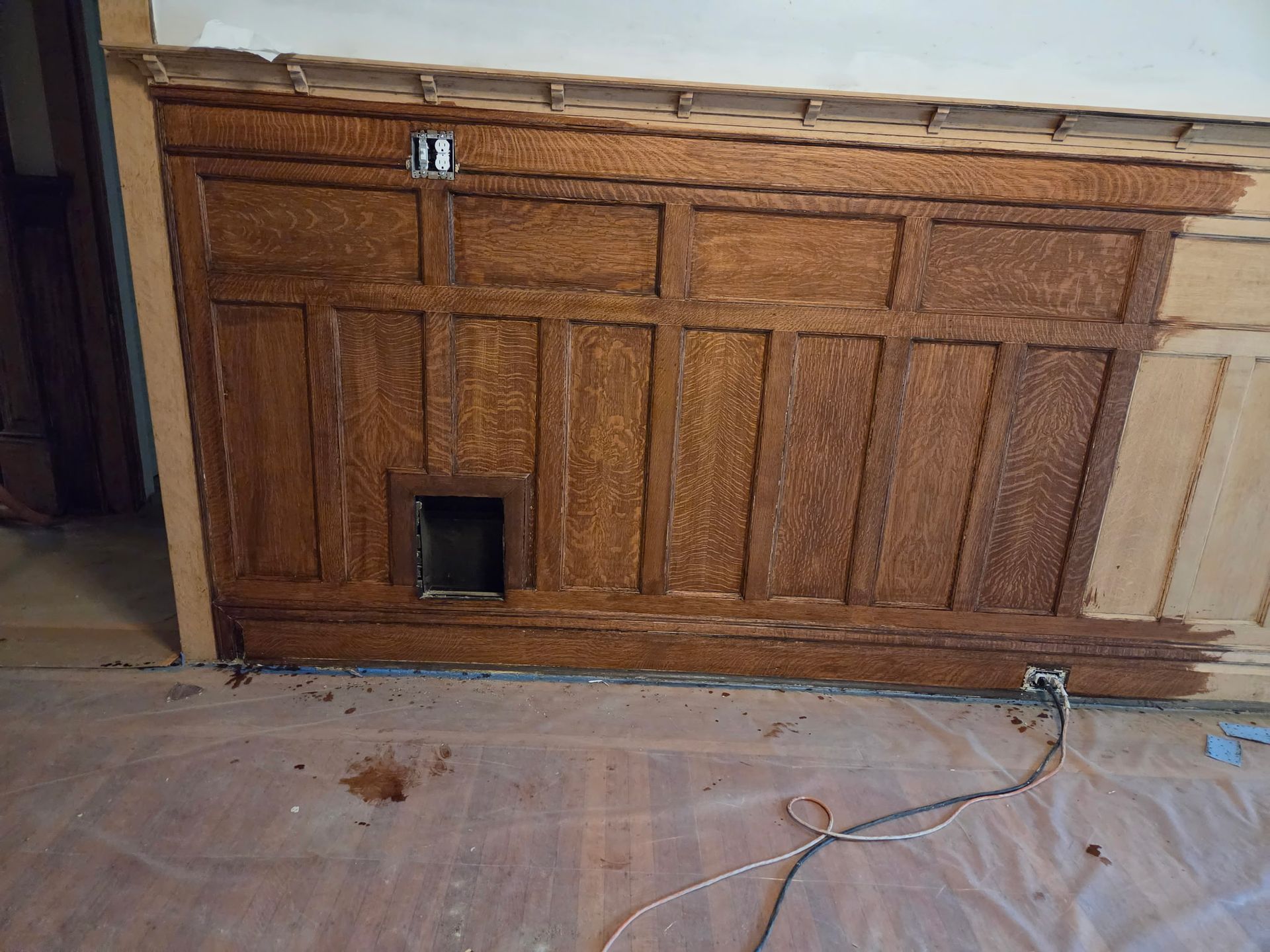 Damaged wooden cabinet or built-in panel with a small opening near the floor in a dusty room.