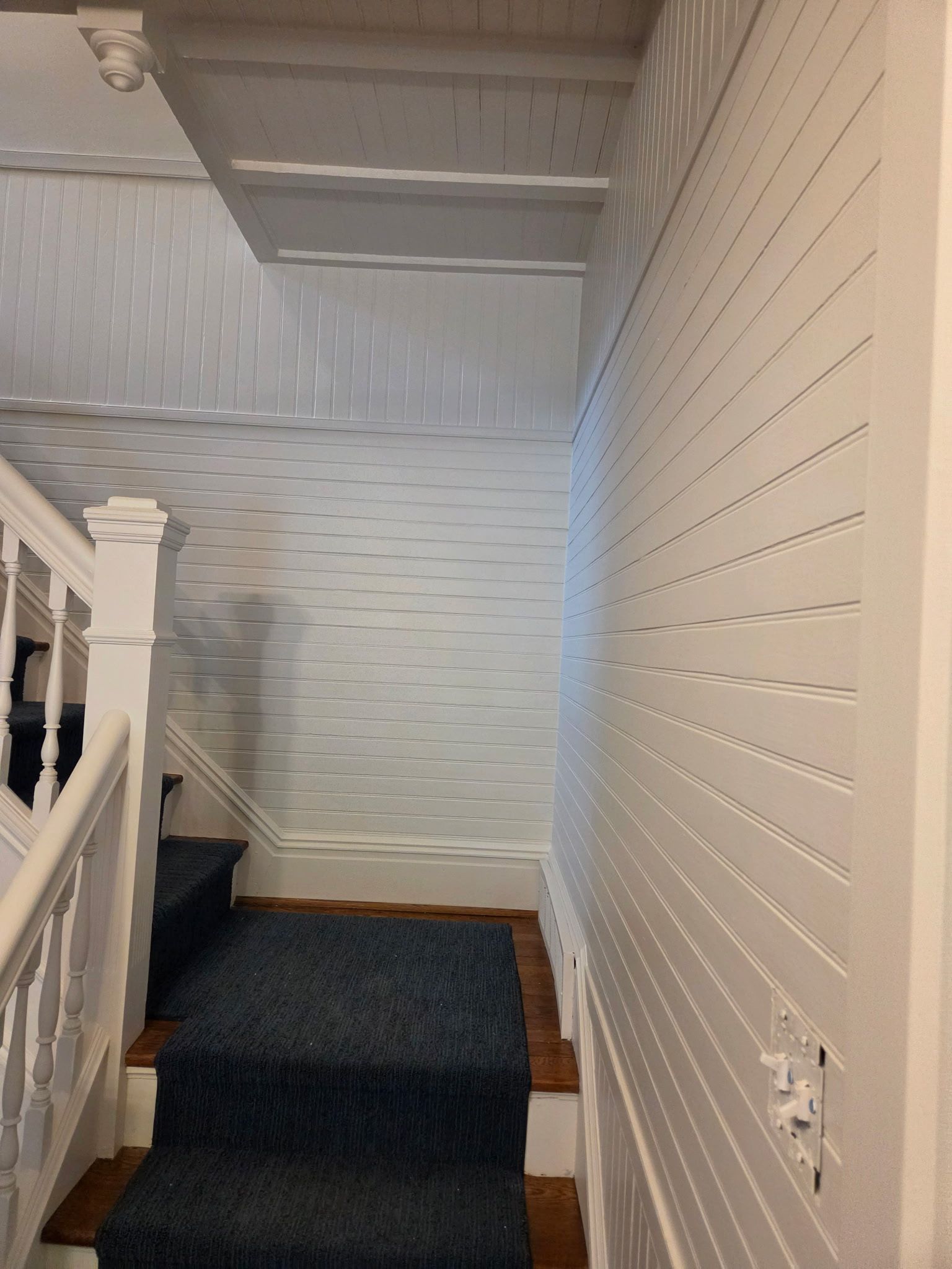 Interior stairwell with white paneled walls, carpeted steps, and a landing under a low ceiling.
