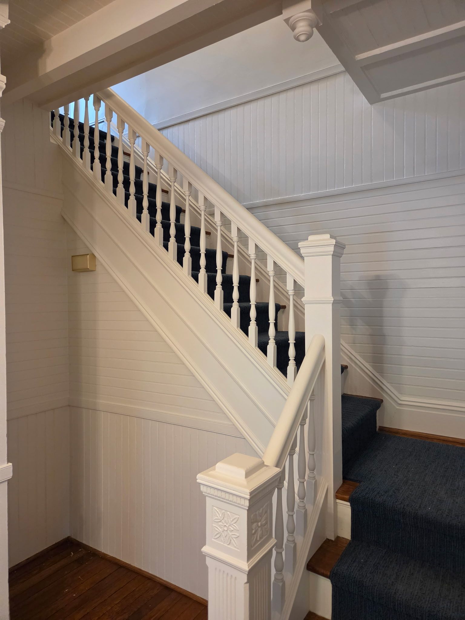 White staircase with ornate banister in a carpeted interior hallway.