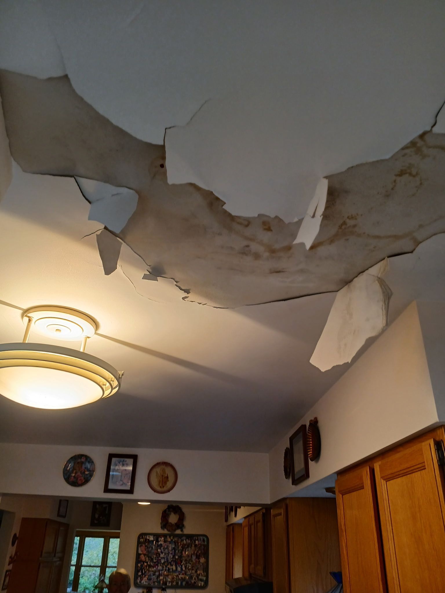 Damaged kitchen ceiling, large sections of drywall peeling away, exposing stained substructure.