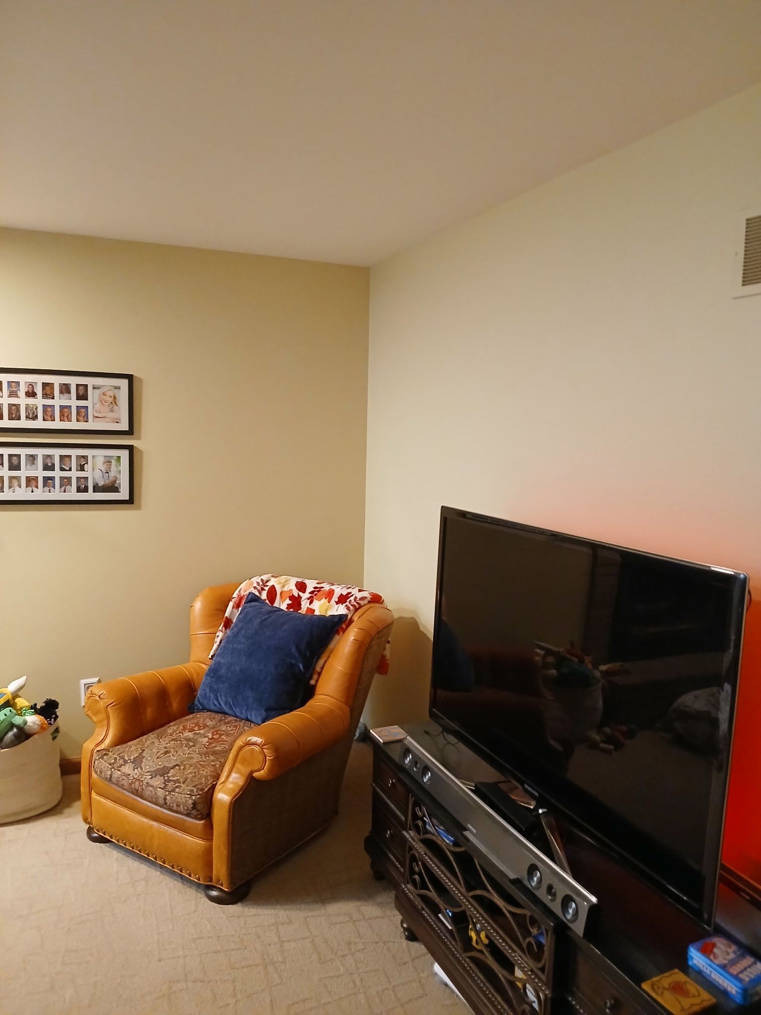 Cozy living room corner with leather armchair, TV, and framed photos on a beige wall.