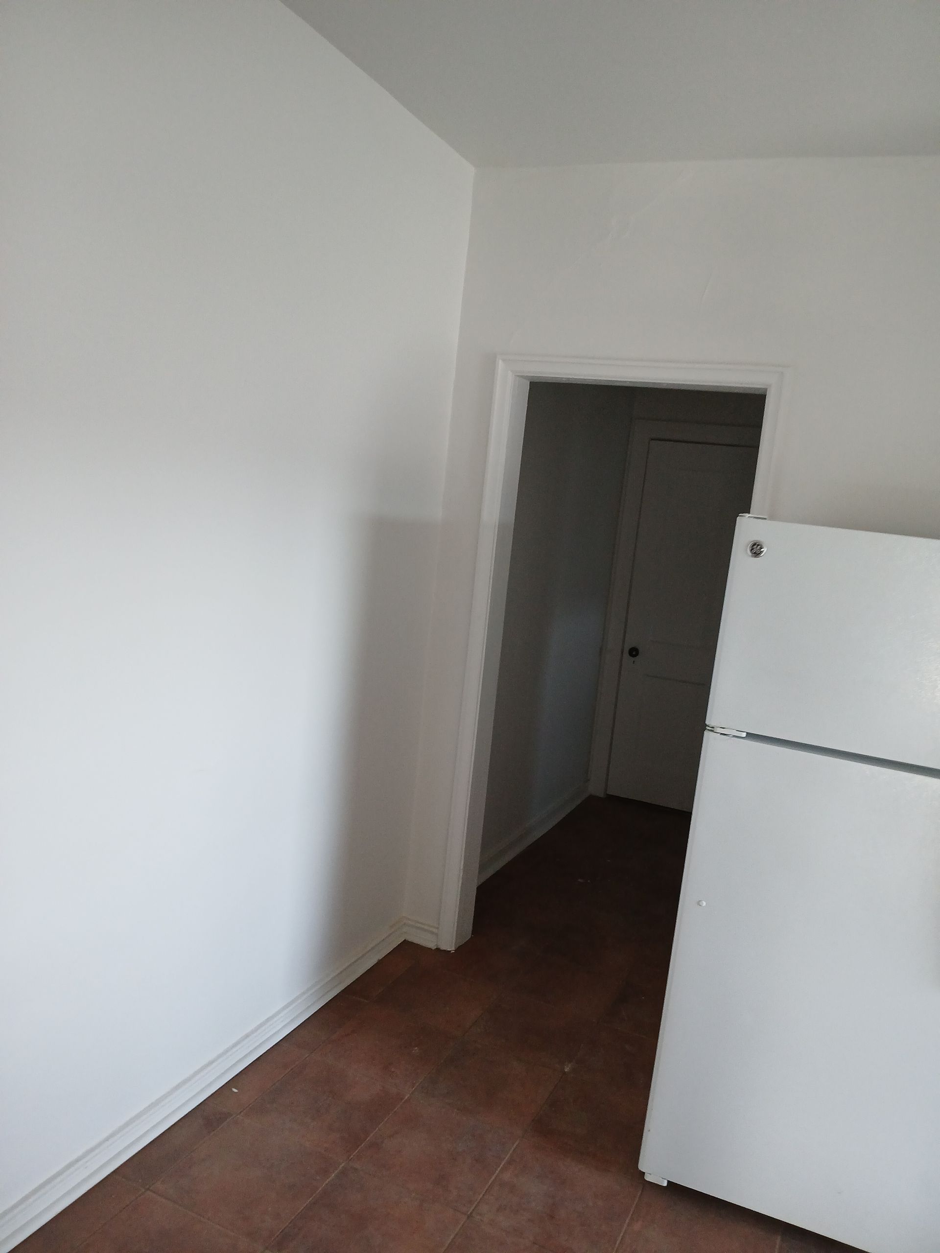 A white refrigerator is sitting in an empty room next to a doorway.