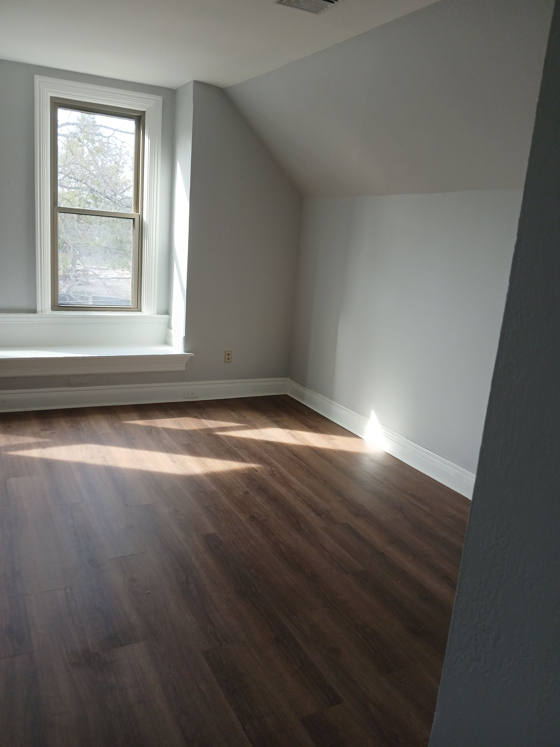 An empty room with hardwood floors and a window.