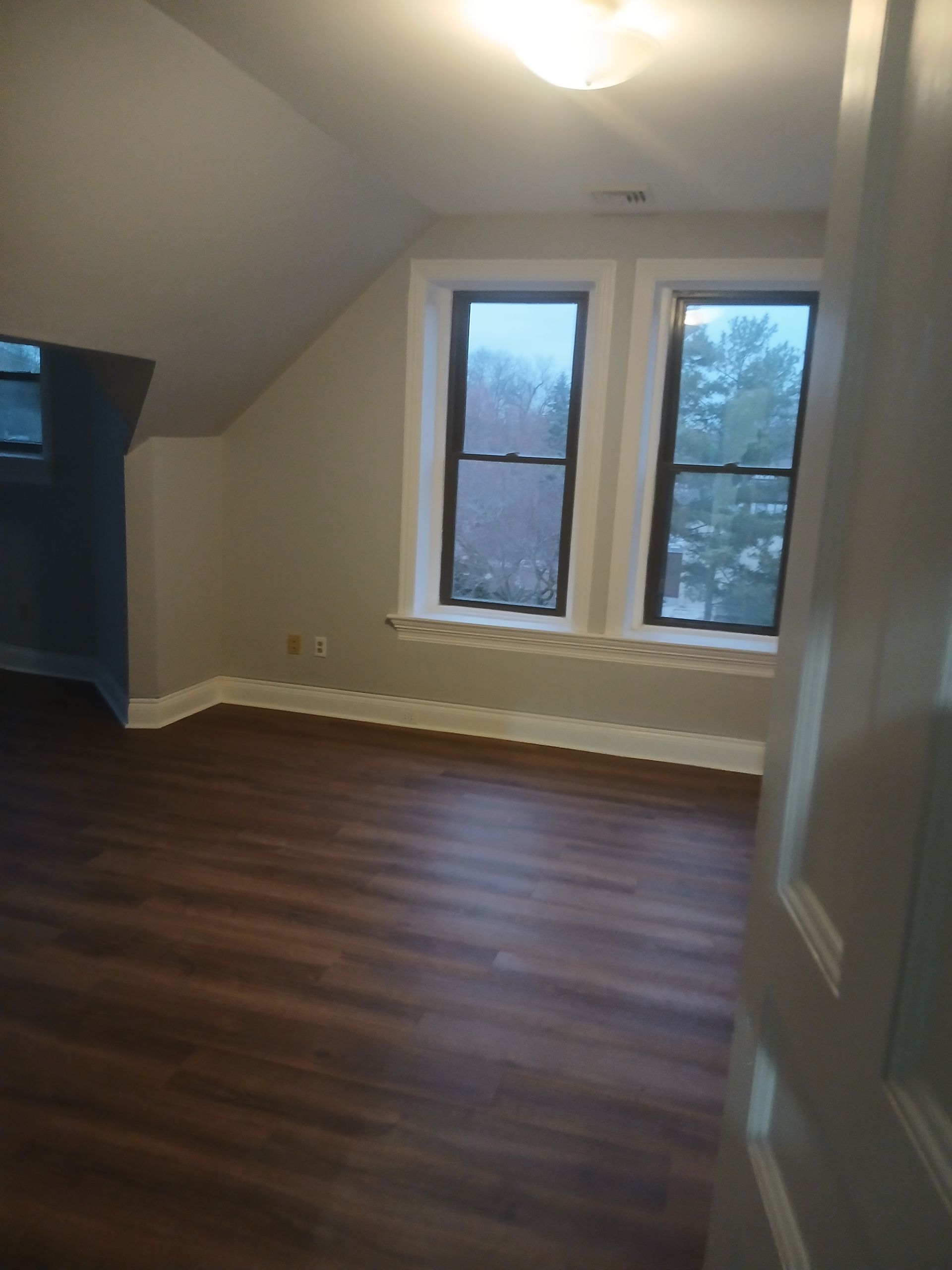An empty room with hardwood floors and three windows.