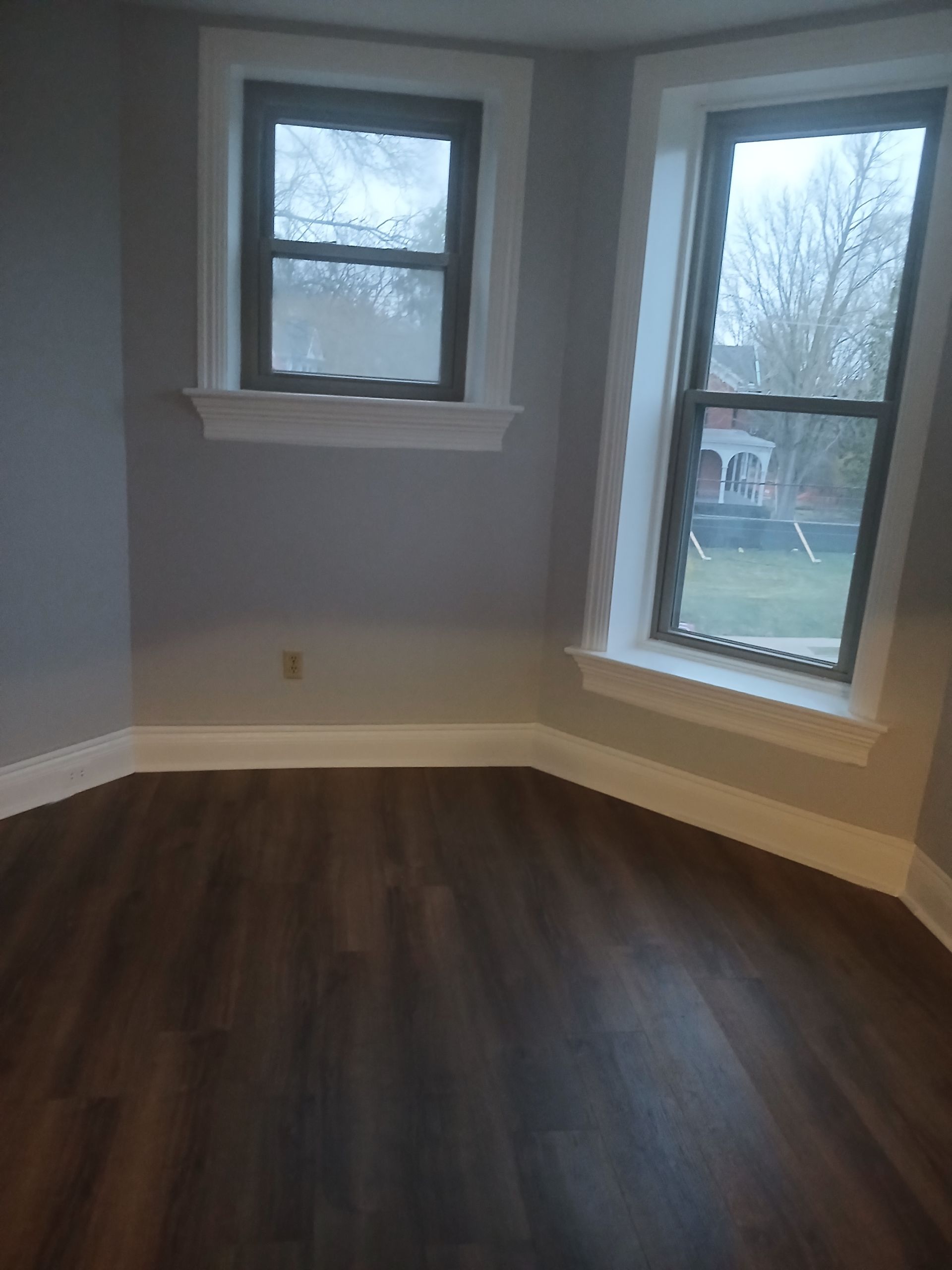An empty room with hardwood floors and two windows.