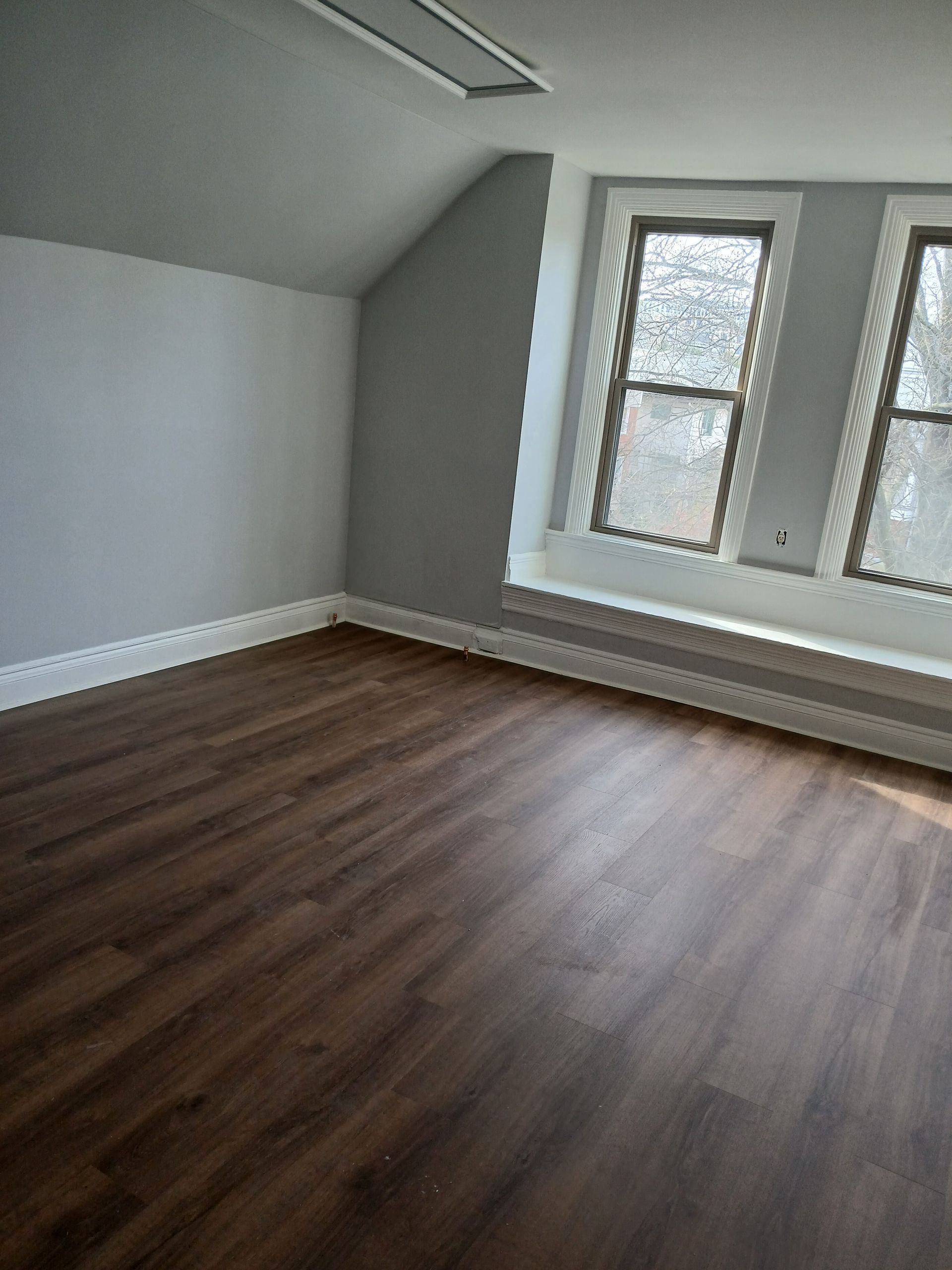 An empty room with hardwood floors and two windows.