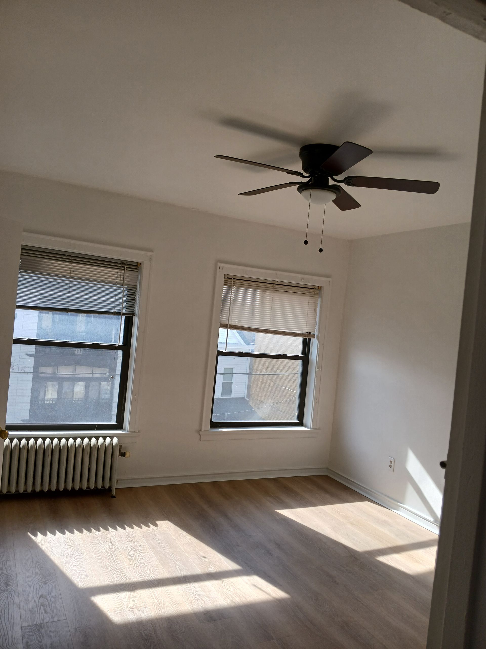 An empty room with a ceiling fan and two windows