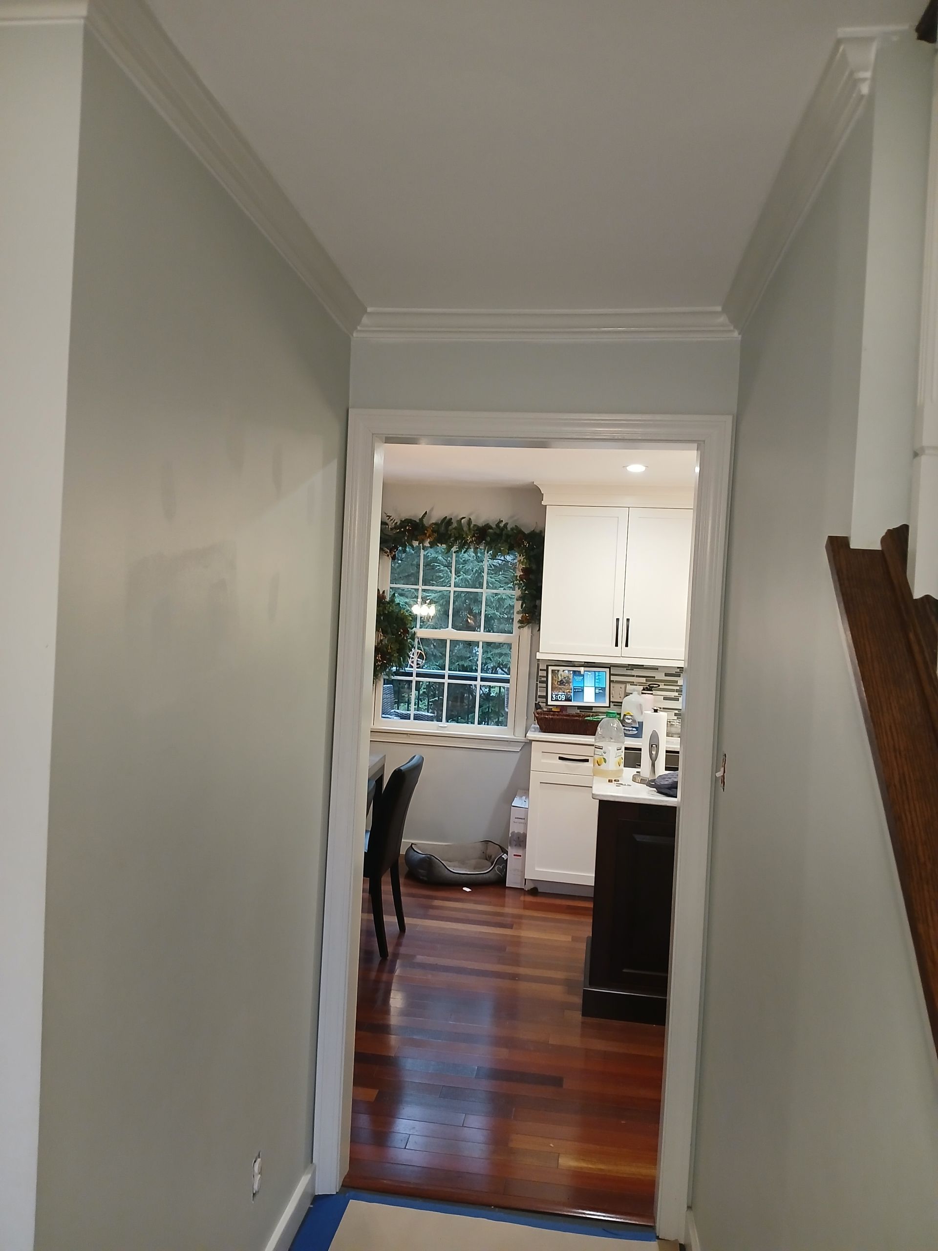 A hallway leading to a kitchen with white cabinets and hardwood floors.