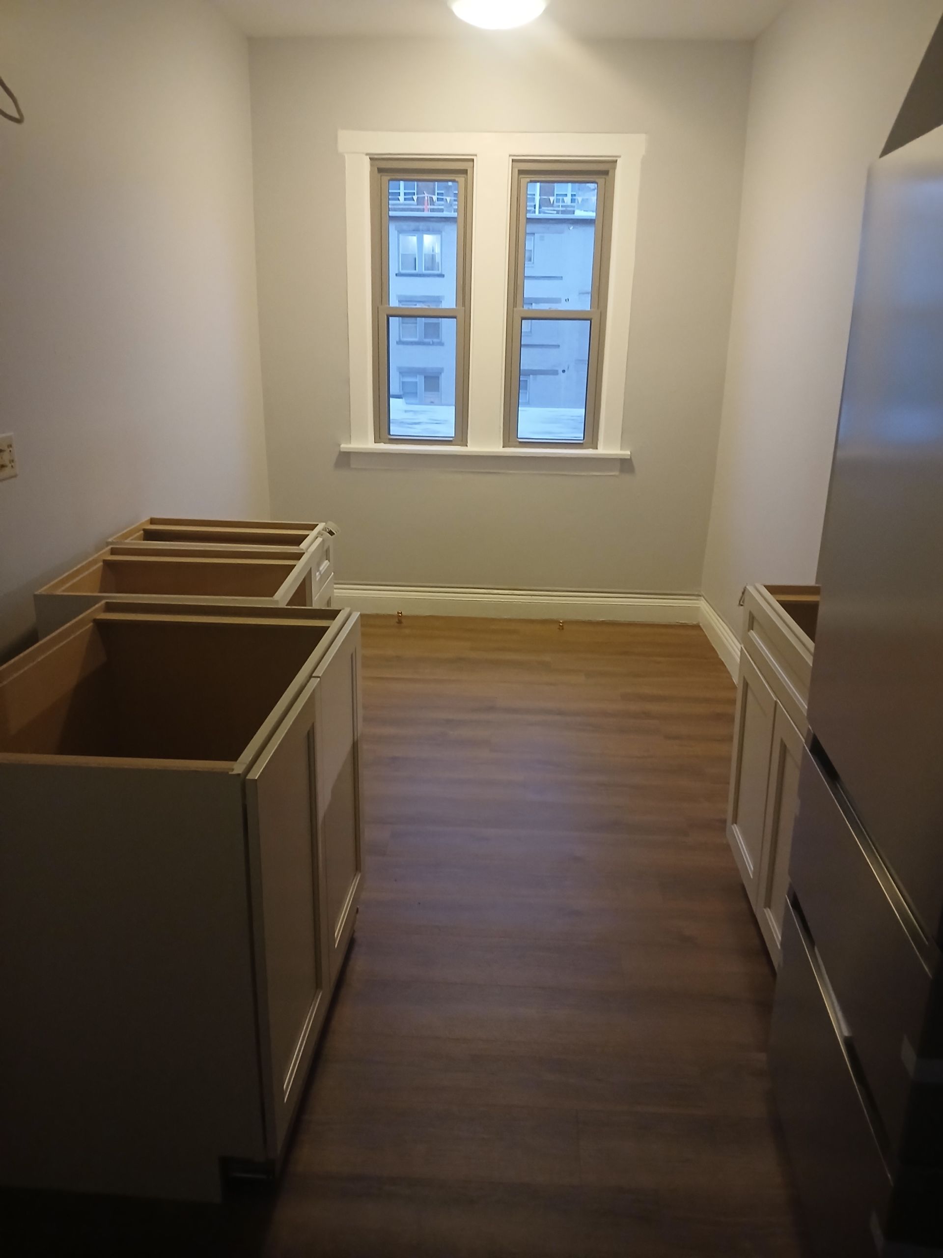 A kitchen with a refrigerator , sink , cabinets and two windows.