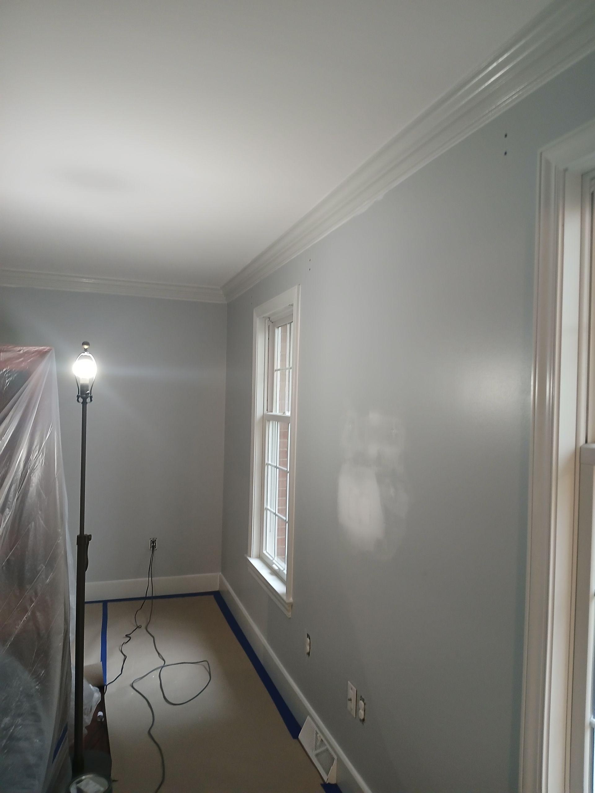 A room with gray walls and white trim is being painted.