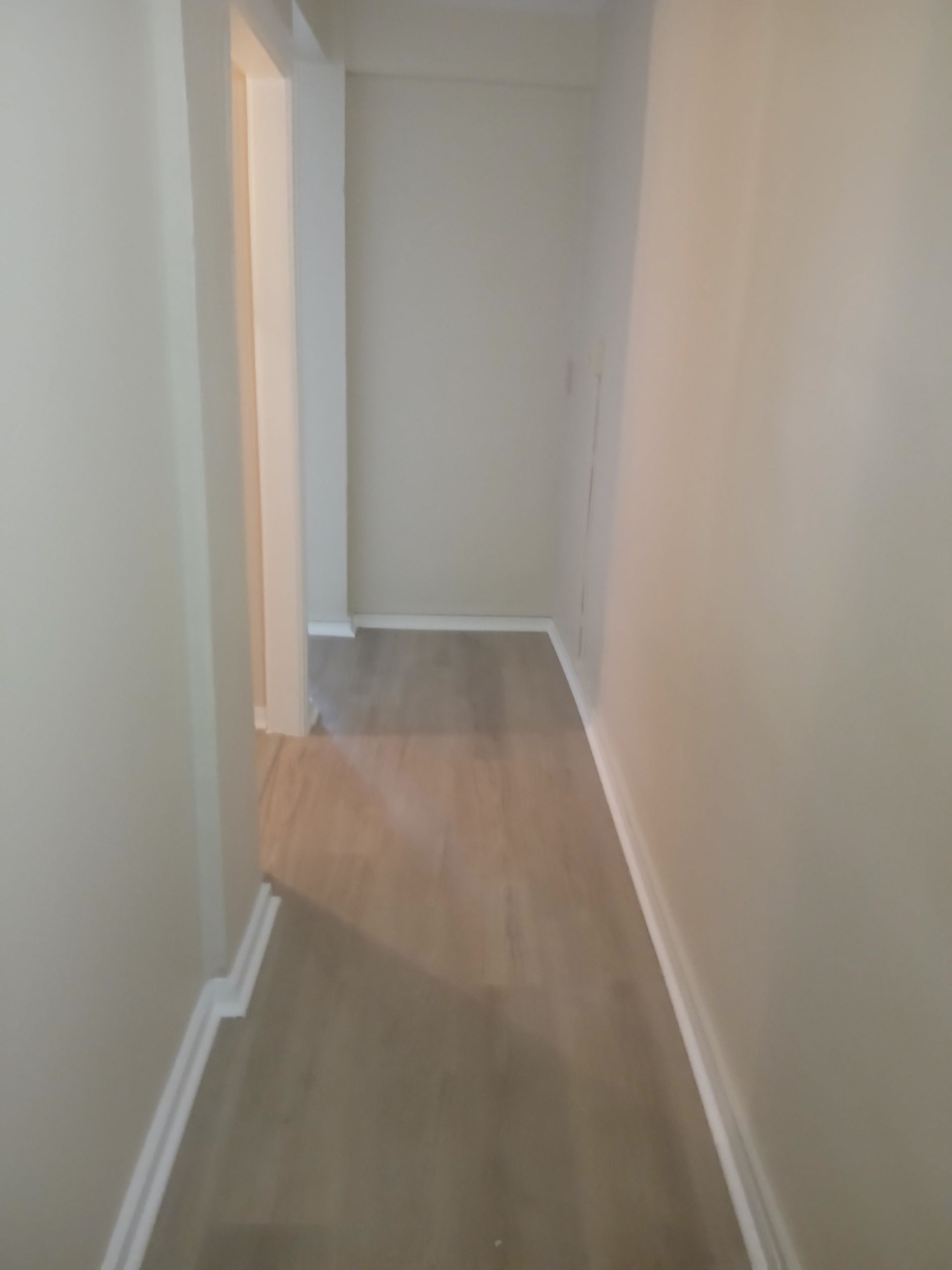An empty hallway with hardwood floors and white trim in a house.