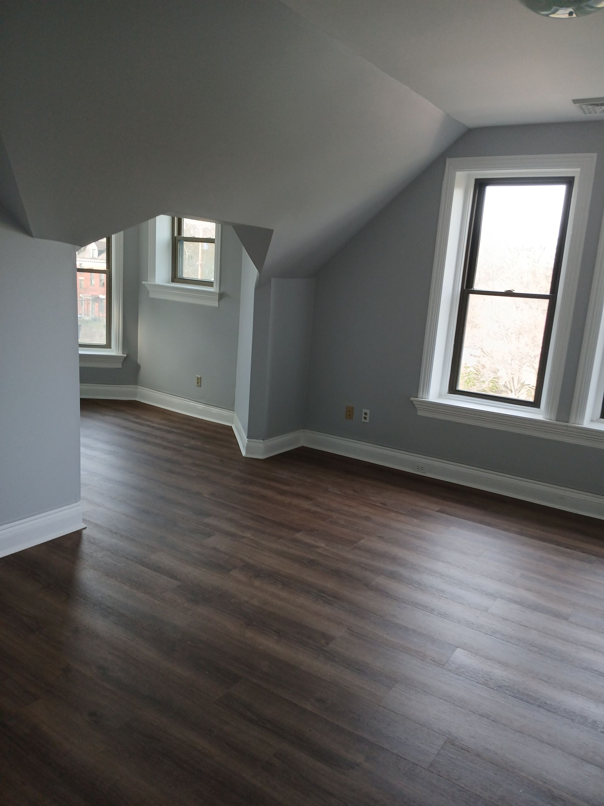 An empty room with hardwood floors and three windows