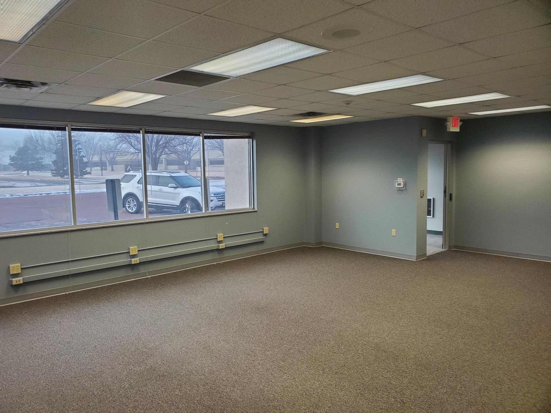 Empty office space with large windows, gray walls, and brown carpet.