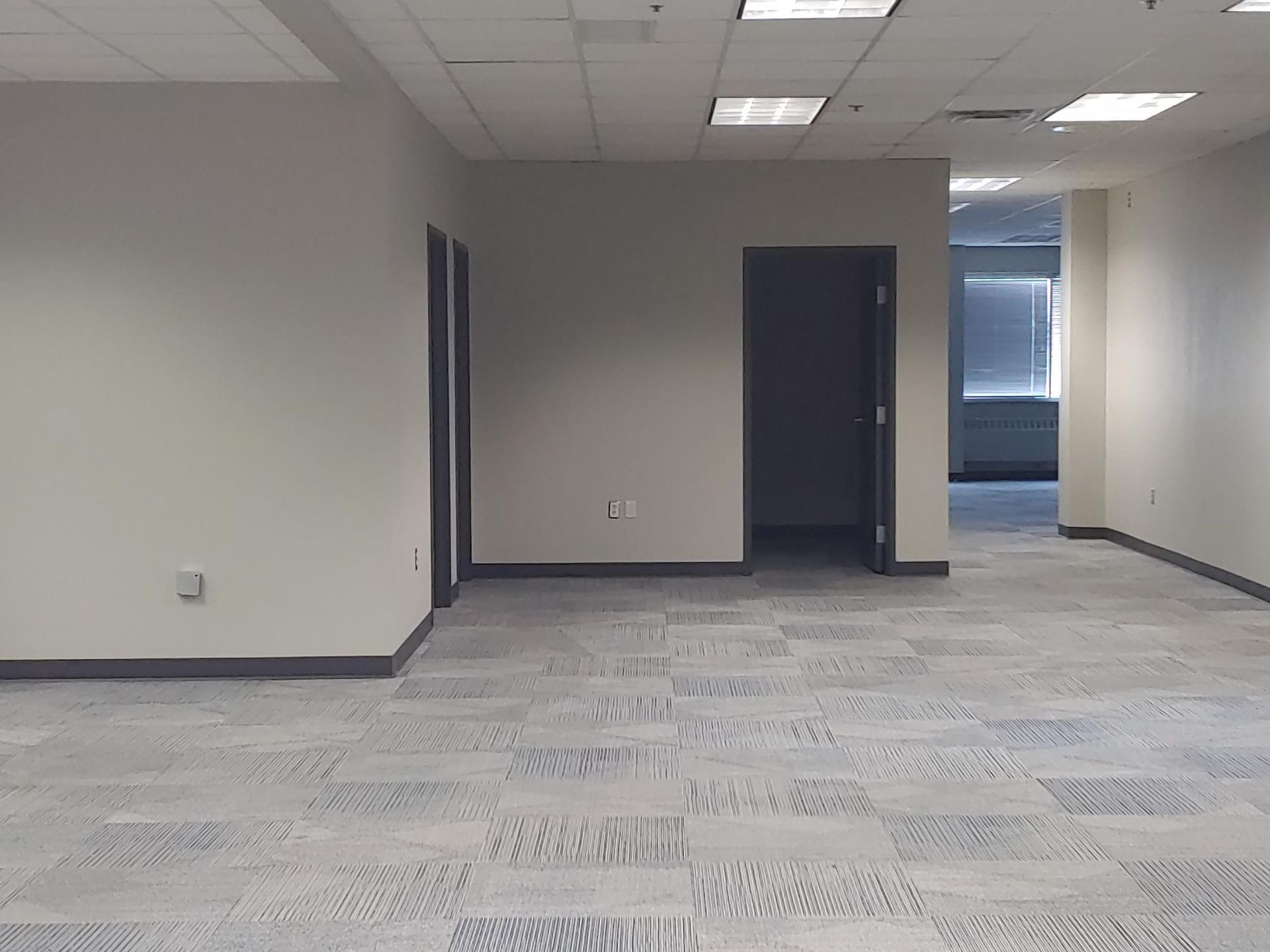 Empty office space with gray carpet, white walls, and open doorways.