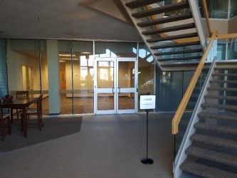 Hallway with glass doors and a staircase. A sign stands near the doors.