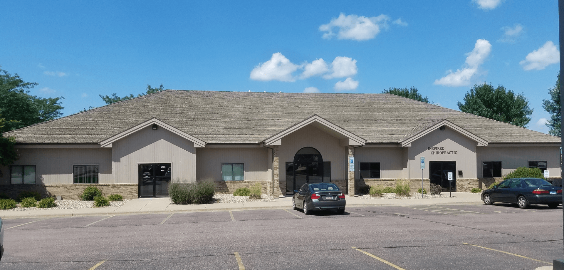 A beige building with a gray roof and black vehicles parked in front. Blue sky.
