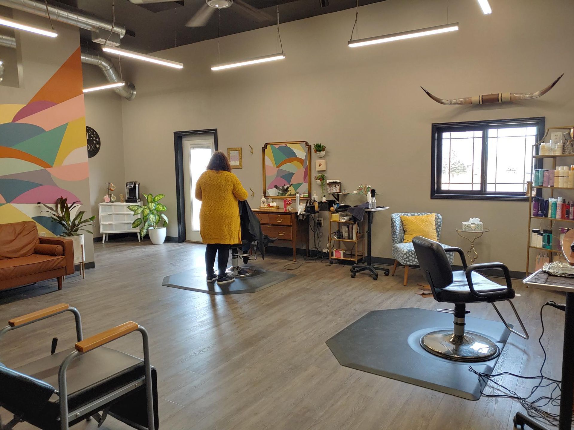Hair salon interior with stylist working on a client. Wooden floors, colorful wall art, and chairs.