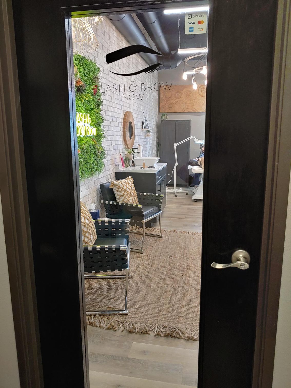 View through an open black door into a beauty salon.  A seating area with chairs and a green wall are visible.