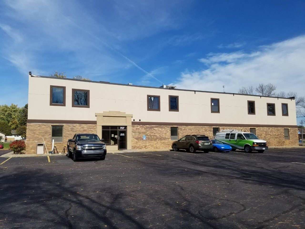 Long, beige commercial building with several windows and a dark parking lot. Several vehicles parked in front.