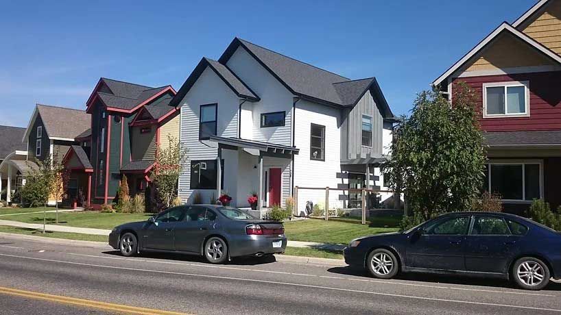 A row of houses with cars parked in front of them on a sunny day.