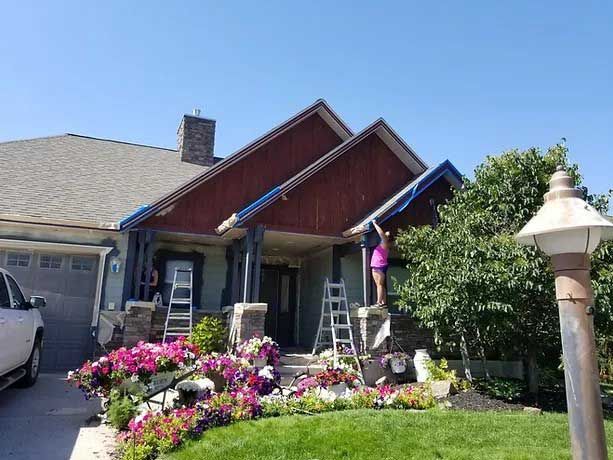A woman is standing on a ladder in front of a house.