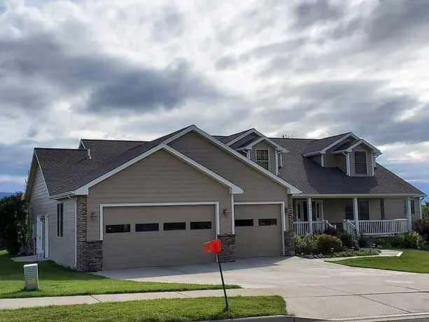 A large house with two garage doors and a porch on a cloudy day.