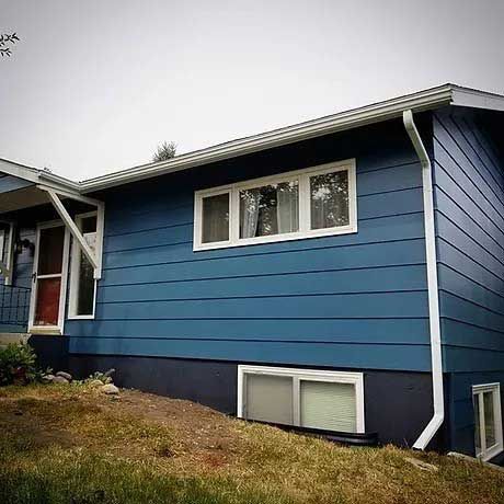 A blue house with white windows is sitting on top of a grassy hill.