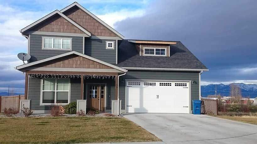 A large house with a white garage door and mountains in the background.