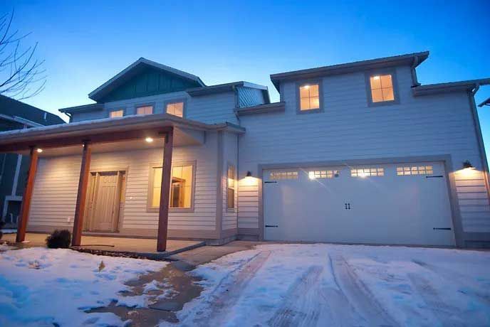 A large white house with a garage and a porch in the snow.